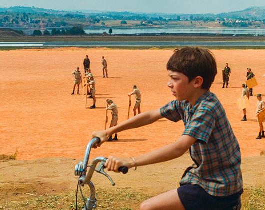 young boy cycling with expanse of red earth and mountains in the background