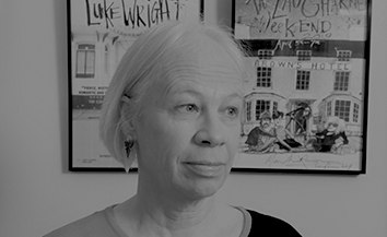 Black and white image of woman with short white bobbed hair, framed posters in background