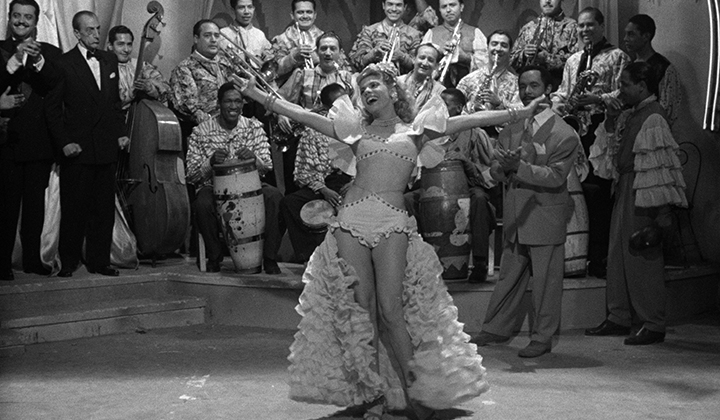 Black and white image of blonde dancer in cabaret costume with plumes, arms outstretched in dance.