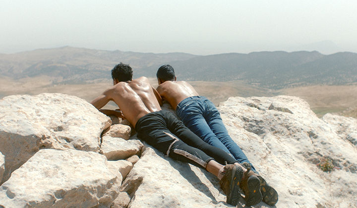 Two teenage boys lying face down on a rock in the sun gazing at landscape below