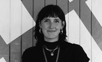 Young white woman with short dark hair wearing blacktop, patterned black and white backdrop 