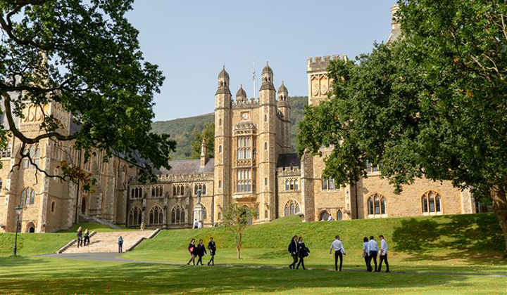 Stone buildings with turrets, with lawns in foreground and outline of hills in background