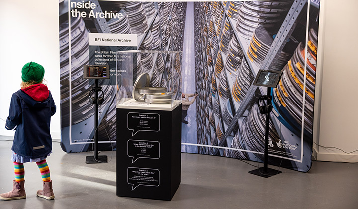 Young girl walking in from of a large Inside the Archive display panel with a glass case in front
