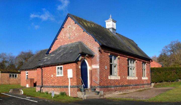Red brick traditional village hall with gabled roof. Blue sky.