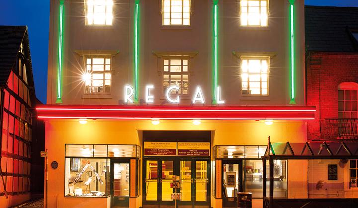 Cinema exterior (signage: Regal) at night, lit up with green and red neon lighting