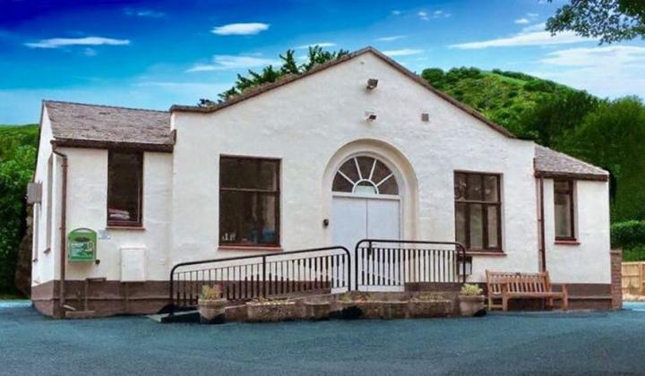 single storey brick village hall painted cream. Hills behind.