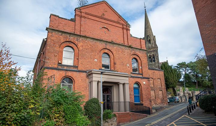 Two-storey Victorian red brick building with portico. Church spire in background.