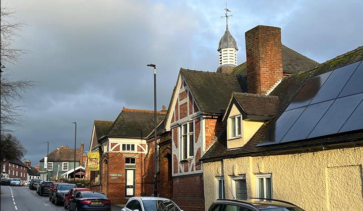 Red brick building with cupola on high street with parked cars