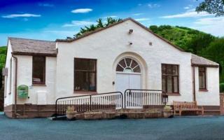 single storey brick village hall painted cream. Hills behind.