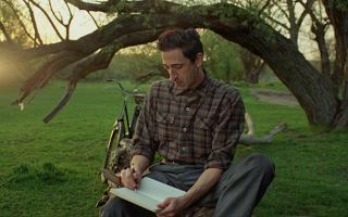 Man wearing checked shirt sitting in garden under a tree sketching