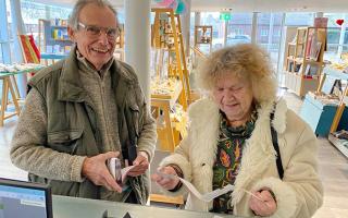 Older white man smiling next to older white woman with curly hair examining tickets