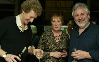 Smiling woman standing between two men, drinking wine