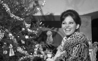 Young woman in fur coat smiling next to Christmas tree