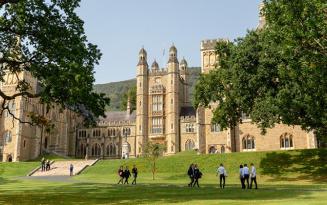 Stone buildings with turrets, with lawns in foreground and outline of hills in background