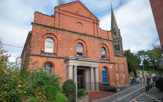 Two-storey Victorian red brick building with portico. Church spire in background.