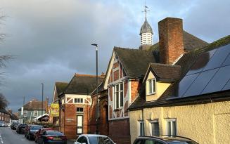 Red brick building with cupola on high street with parked cars