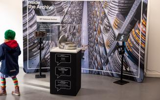 Young girl walking in from of a large Inside the Archive display panel with a glass case in front