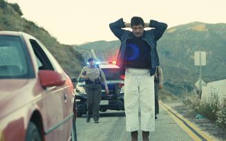 Man in white baggy cropped pants with arms crossed above his head standing g in toad with policewoman