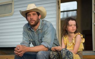 Guy in cowboy hat and blue shirt sitting next to small girl in yellow dress outside white trailer