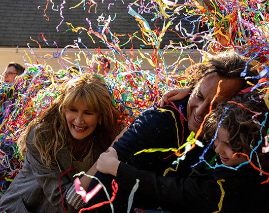 Woman, man and boy gathered together, laughing under multicoloured streamers